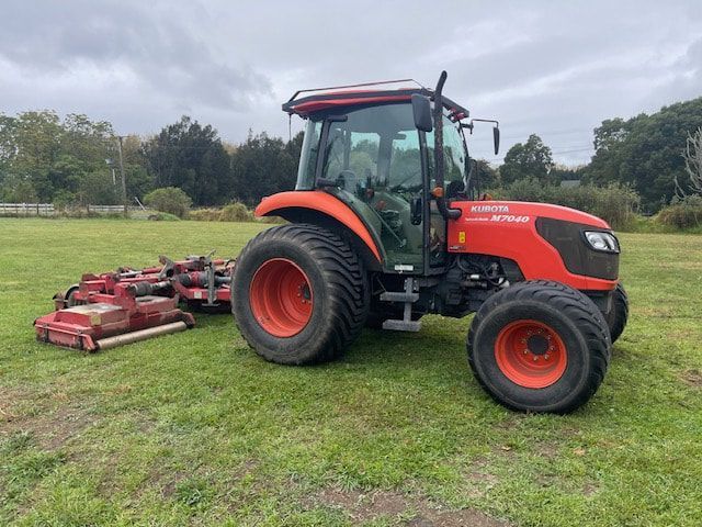 A red tractor is parked in a grassy field with a mower attached to it.