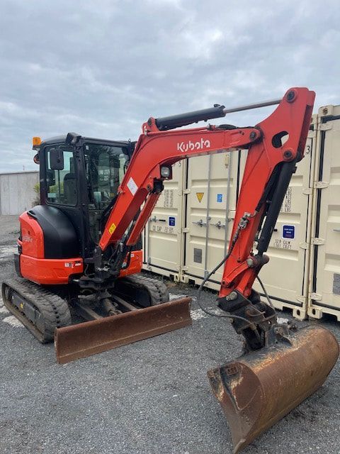 A red excavator is parked in front of a shipping container.