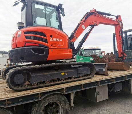 An orange excavator is parked on top of a flatbed truck.