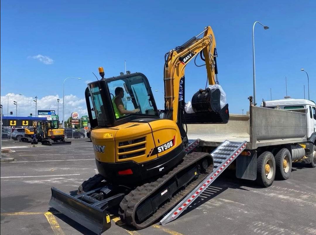A yellow excavator is being loaded onto a dump truck.