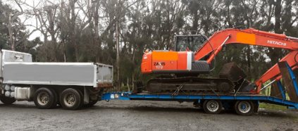 A large excavator is being towed by a flatbed truck.