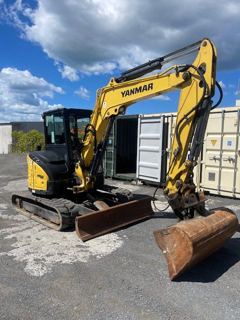 A yellow yanmar excavator is parked in front of a shipping container.