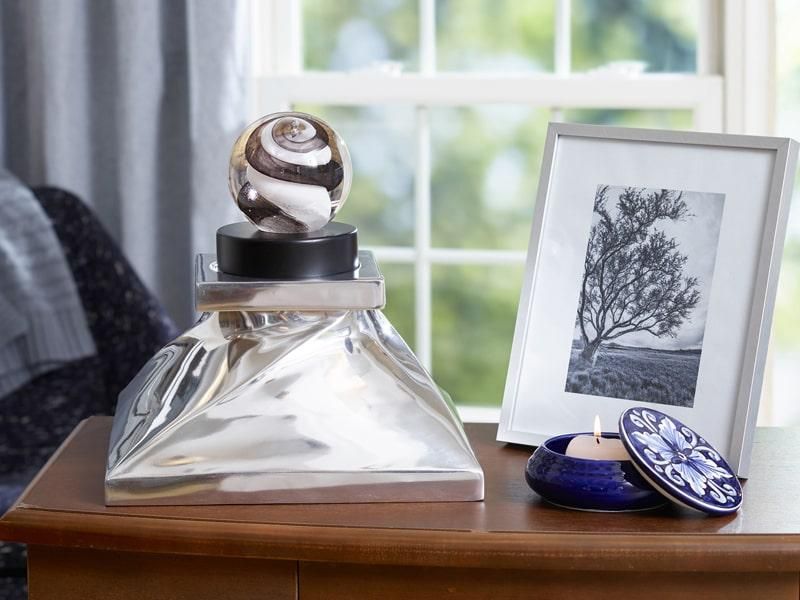 Silver sculpture with a glass orb, framed photo, and a blue candle holder on a table.