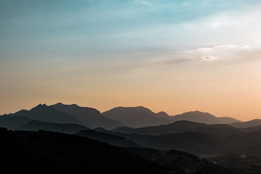 Silhouetted mountain range under a pastel-colored sky; orange and blue hues.