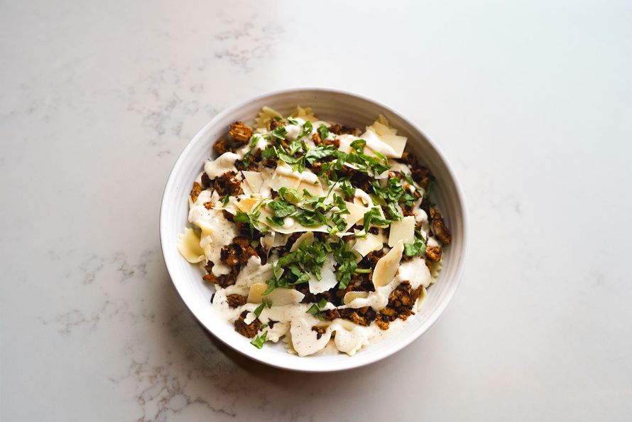 Bowl of rice topped with herbs, vegetables, and sauce on a white table