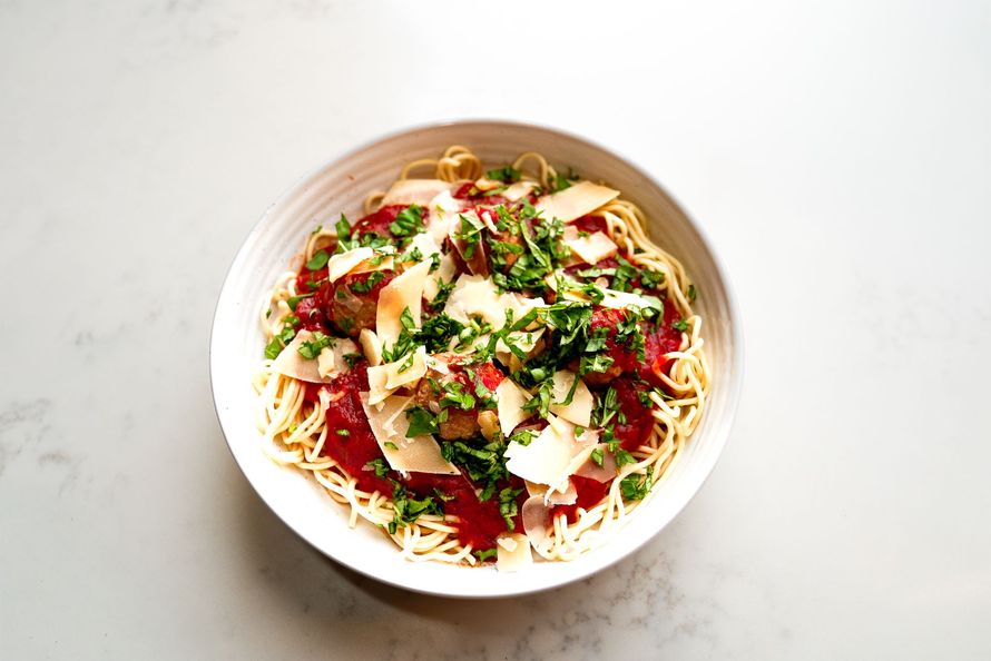 Overhead view of pasta with red sauce, herbs, and shaved cheese in a white bowl