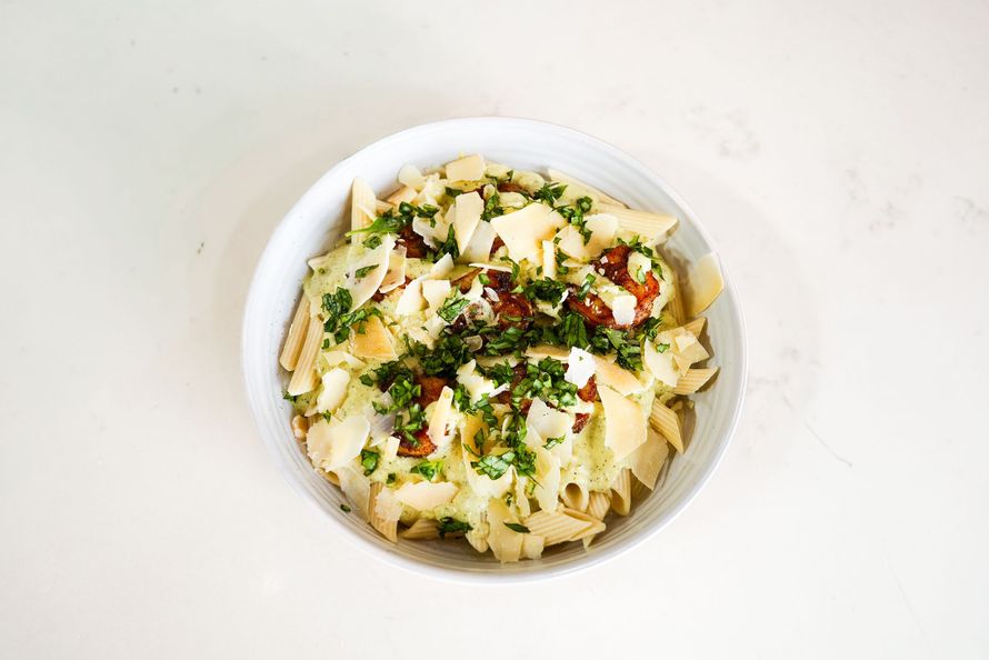 Bowl of pasta with grated cheese, herbs, and red pepper on a white table