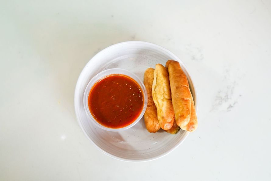 White bowl with red dipping sauce and three golden fried sticks on a light surface