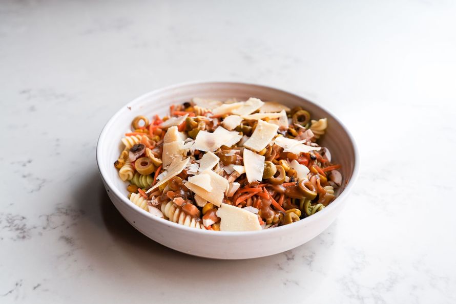 Bowl of pasta salad topped with shaved cheese on a white surface