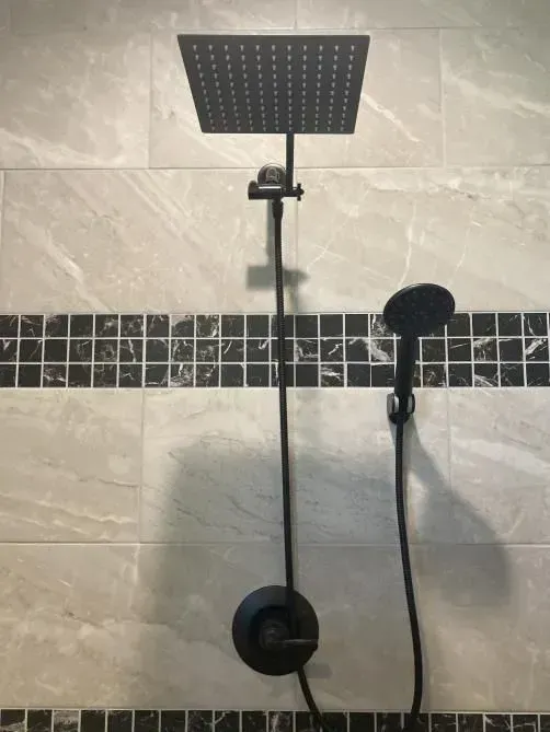 A close up of a shower head and shower head in a bathroom.