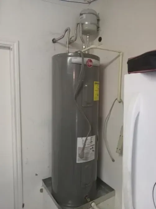 A gray water heater is sitting in a kitchen next to a refrigerator.