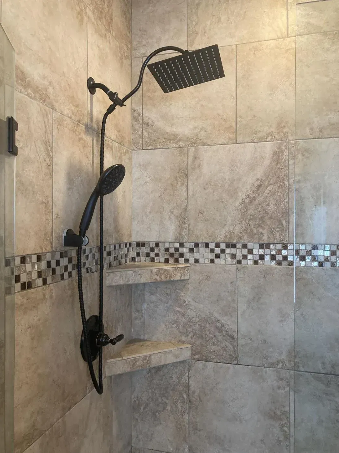 A shower with a black shower head and two shelves.