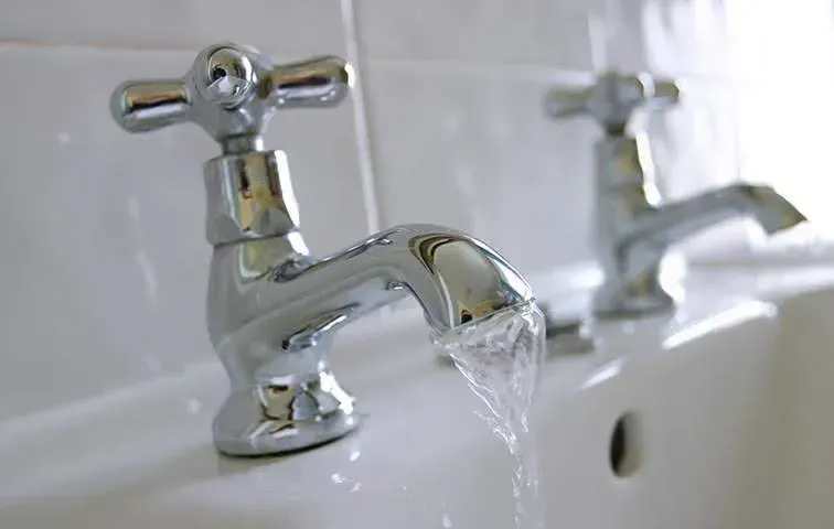 A bathroom sink with two chrome faucets and water running from them.