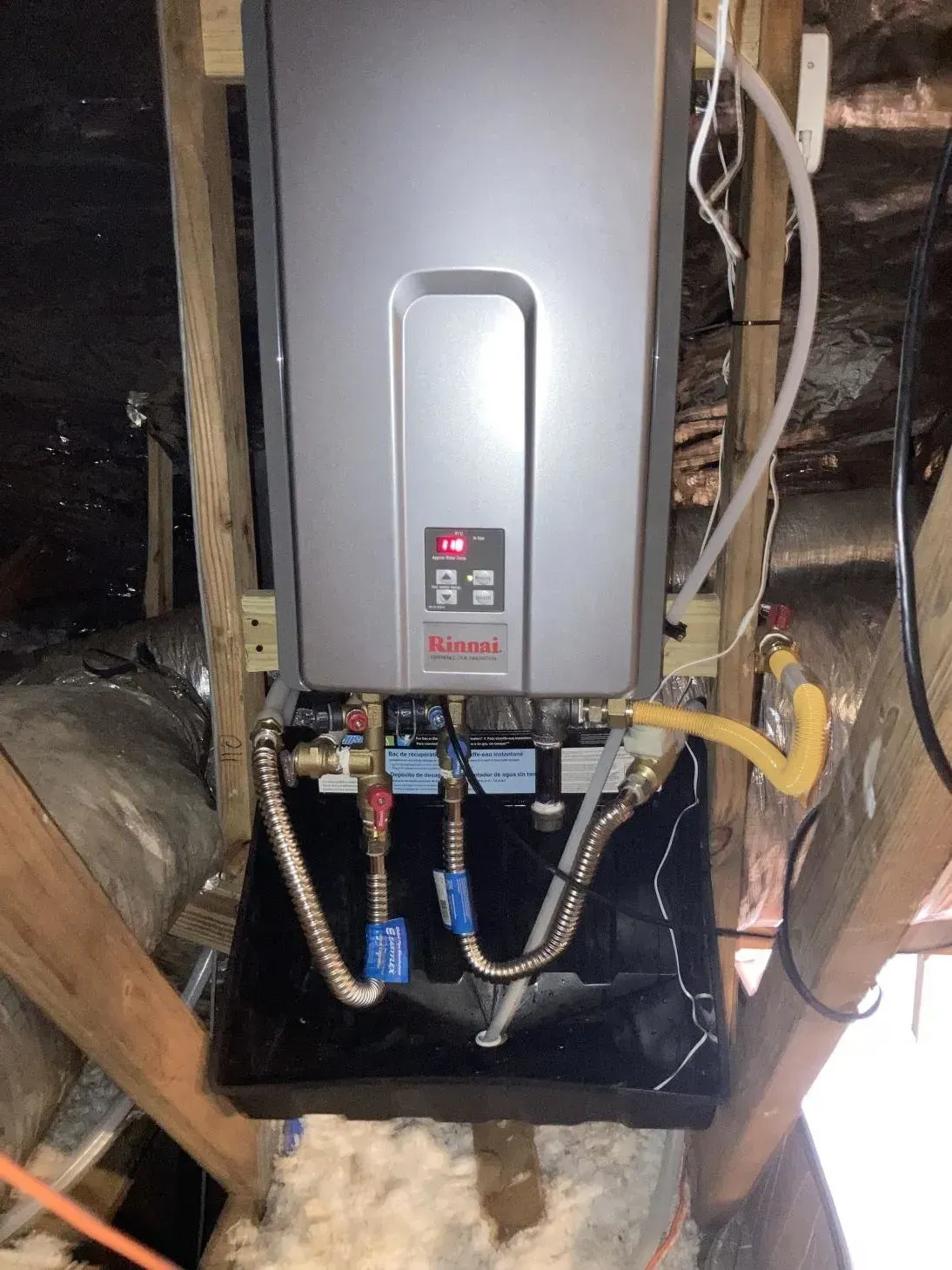A water heater is hanging from the ceiling in an attic.