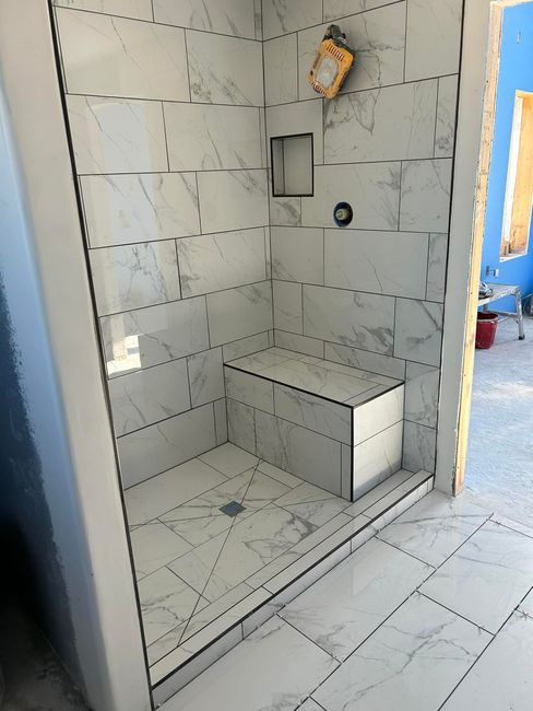 A shower stall with a bench in a bathroom under construction.