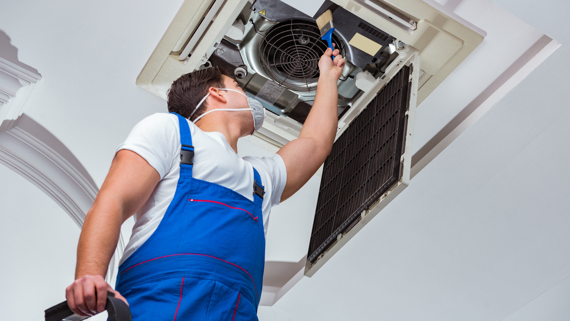 A man wearing a mask is working on an air conditioner.