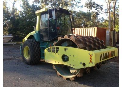 A green and yellow ammann roller is parked on the side of the road