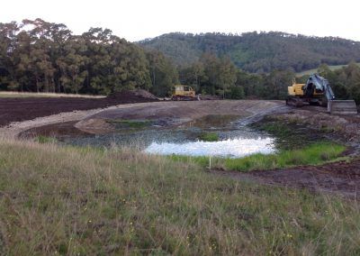 Two bulldozers are working in a field next to a pond.