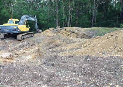A yellow excavator is driving through a dirt field.