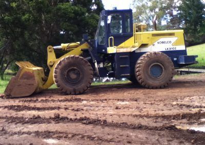 A blue and yellow kobelco bulldozer is parked in a muddy field