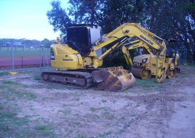 A yellow excavator is parked next to a cat roller in a dirt field.