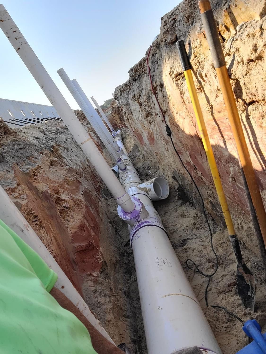 Pipes installed in a trench, with purple primer on joints. Two shovels leaning against the trench wall.