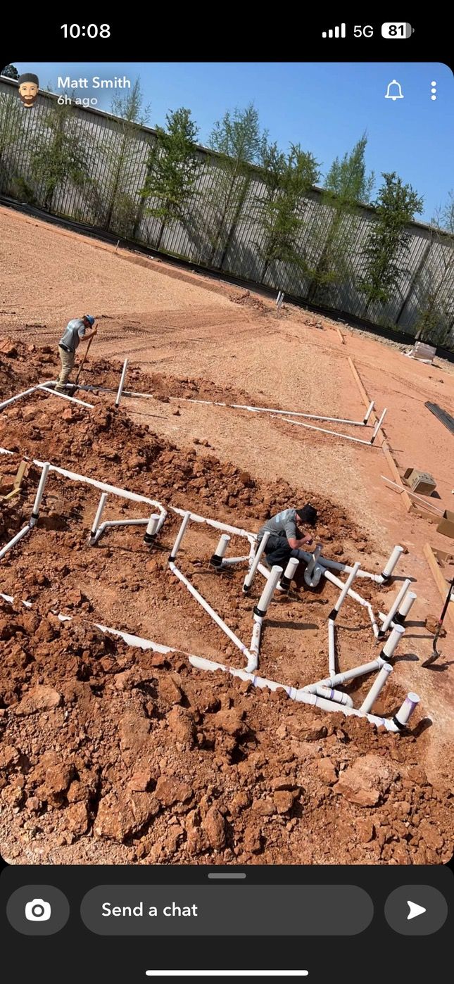 Pipes being installed in a construction site. Brown soil and a fence in the background.