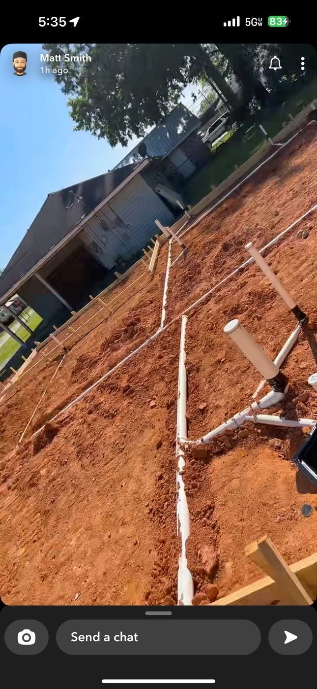 A person laying white PVC pipes in a dirt yard next to a house. Sunny day.