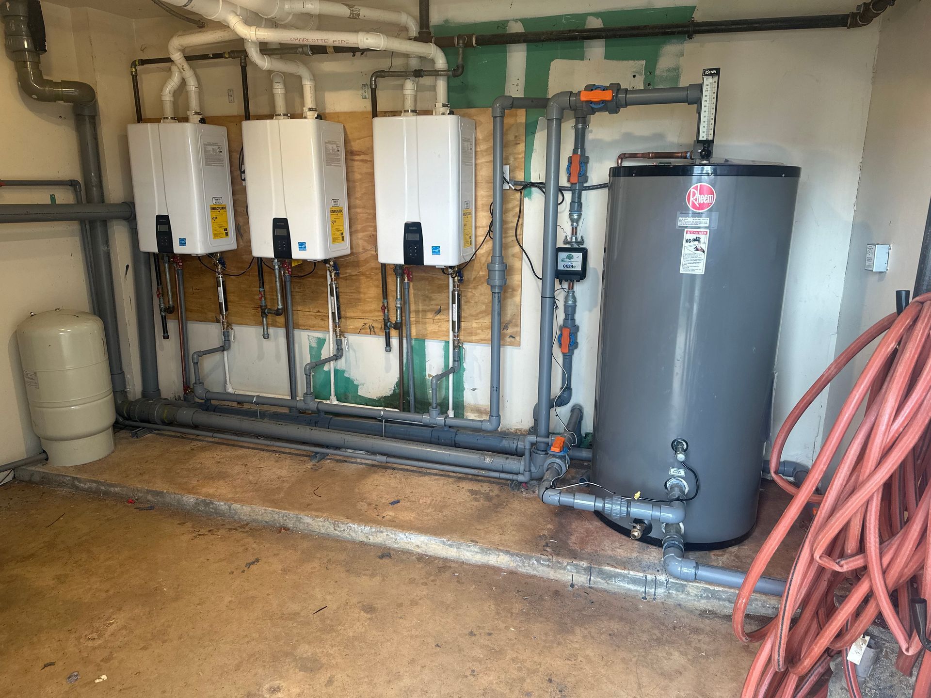 Three white water heaters with a storage tank and plumbing in a utility room.