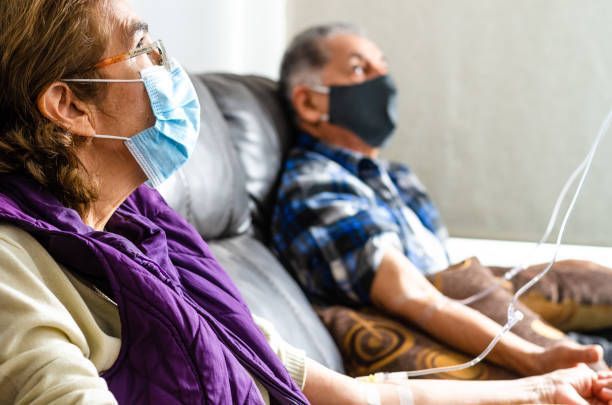 A Man and a Woman Wearing Face Masks are sitting on a Couch | Lenexa, KS | Infuzion Oncology Solutions