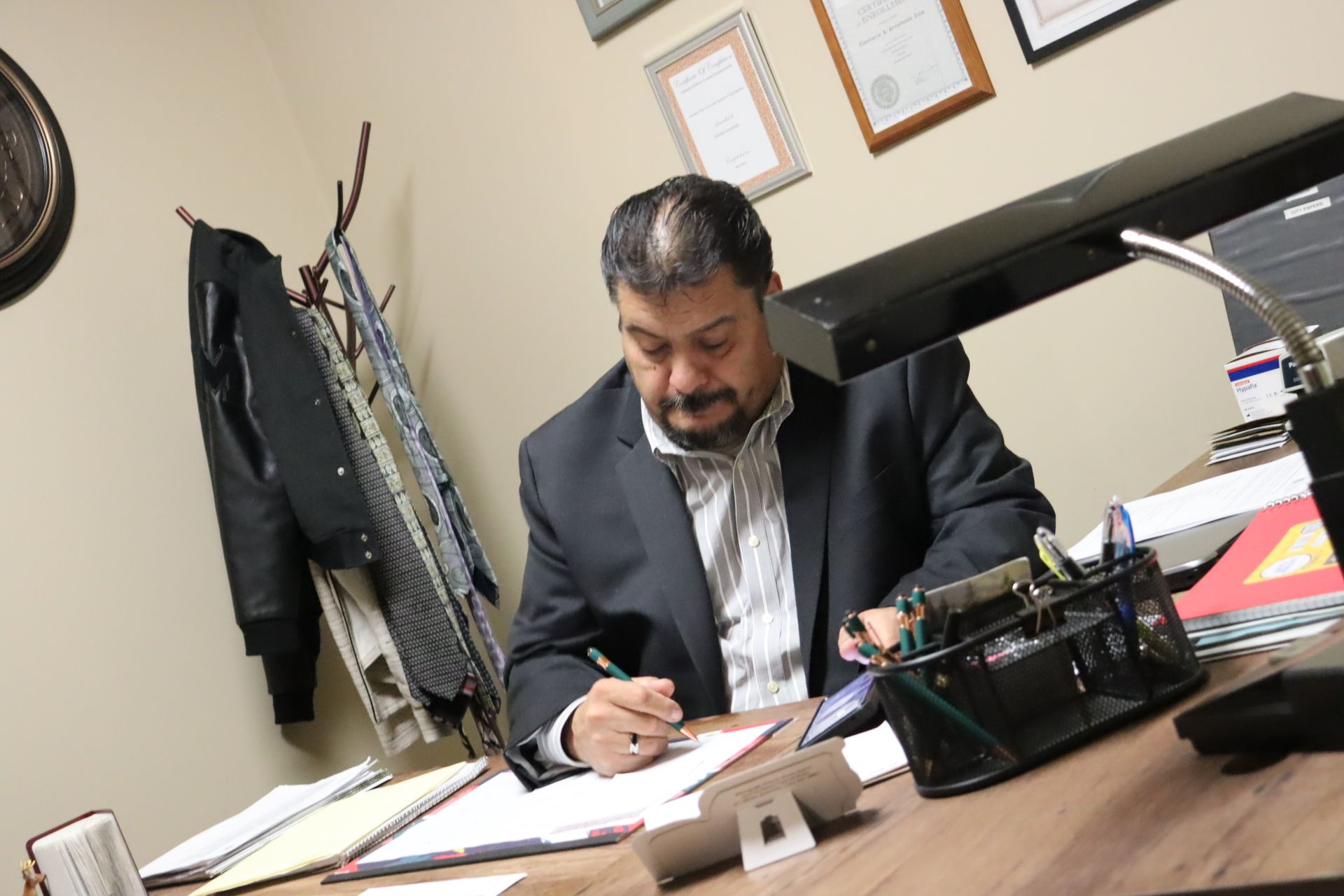 A man in a suit is sitting at a desk writing on a piece of paper.