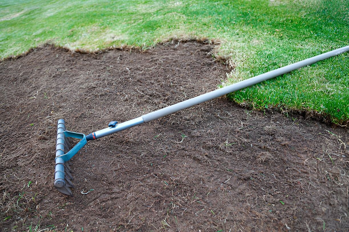A rake is sitting on top of a pile of dirt in a yard.