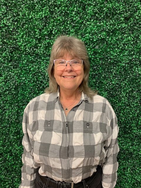 Smiling person in a gray plaid shirt standing against a green leafy background