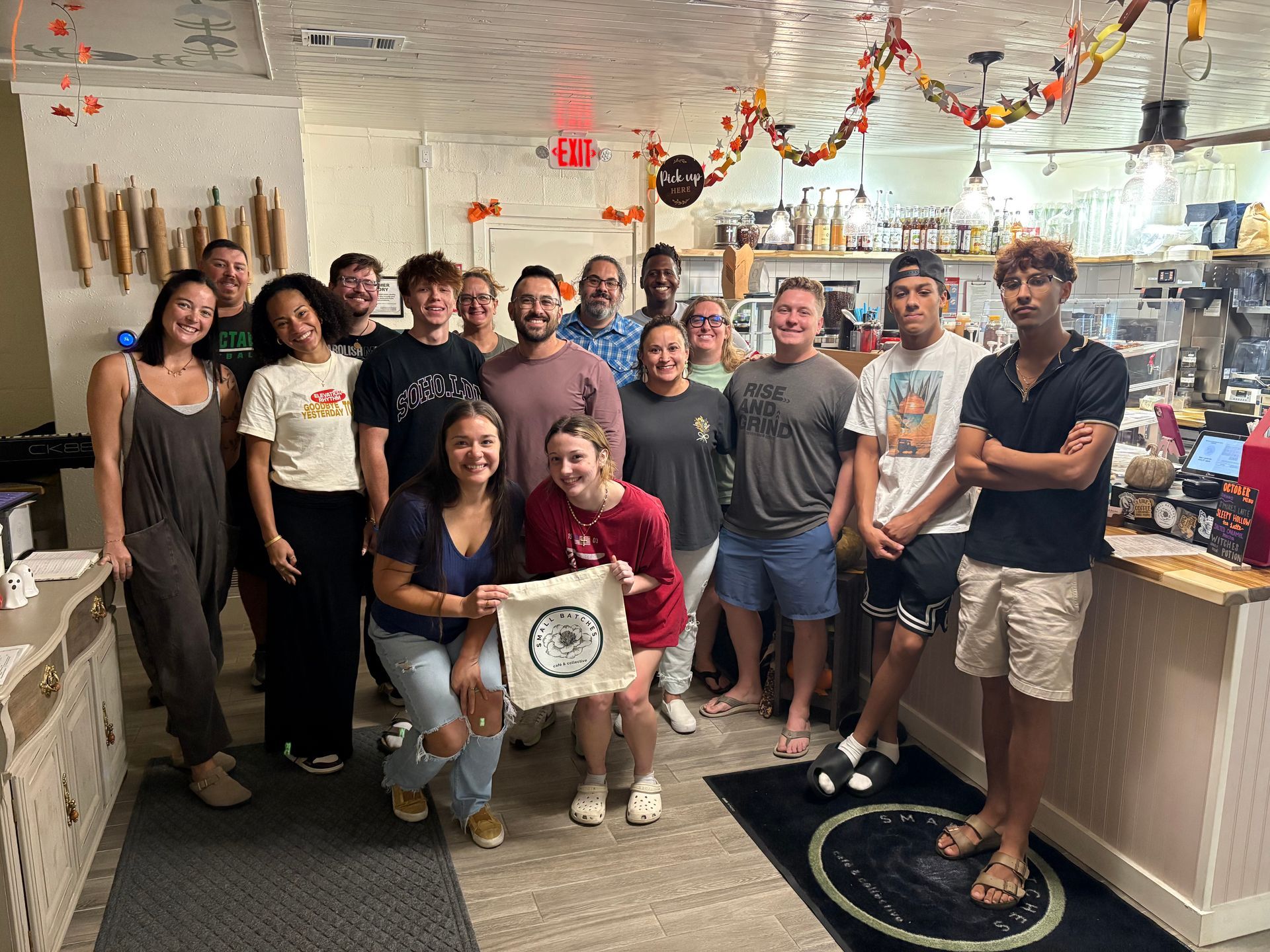 Group of people posing in a decorated kitchen, smiling around a seated person holding a sign.