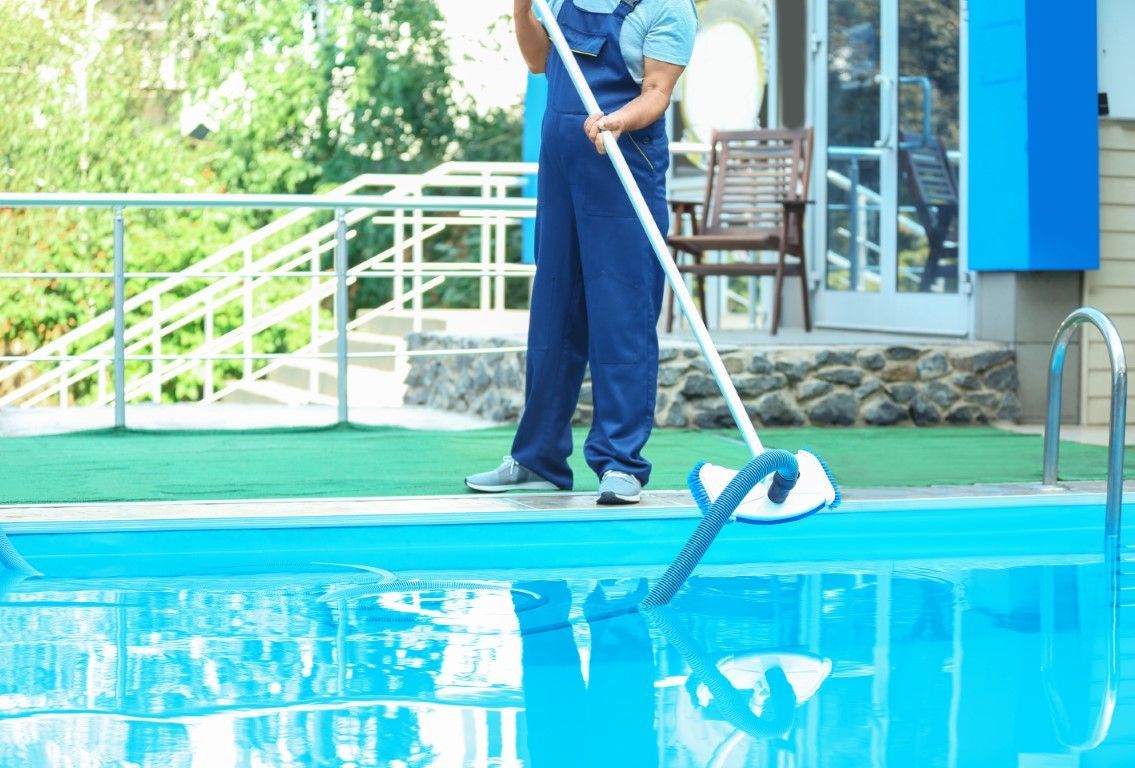 A man is cleaning a swimming pool with a mop.