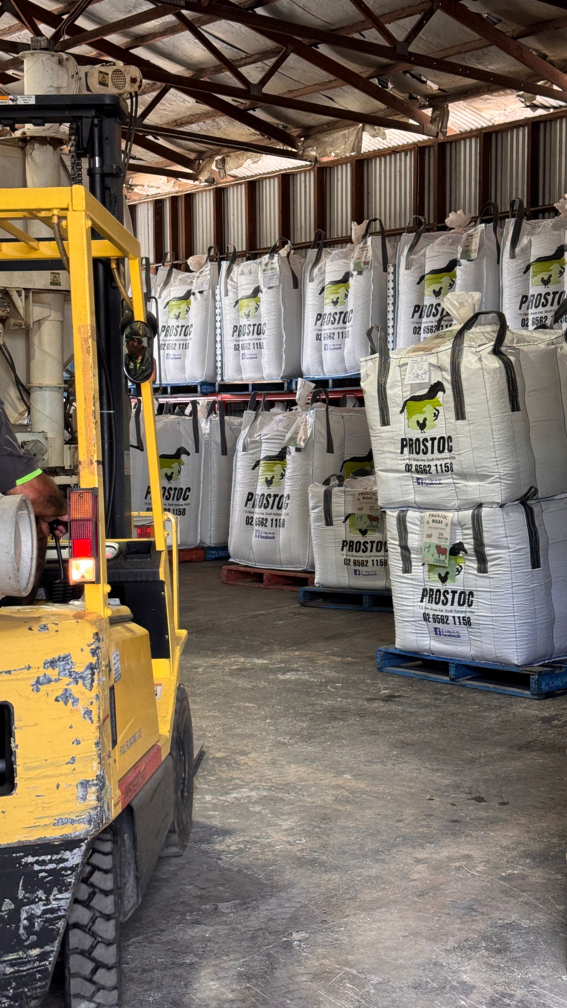A yellow forklift parked in a warehouse beside several rows of stacked, palletized white industrial bags. — Prostoc In South Kempsey, NSW