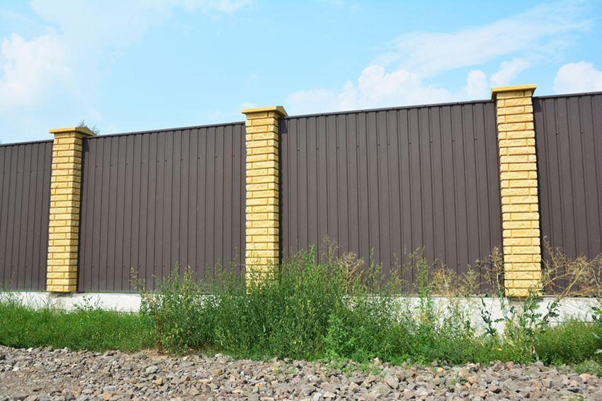 A Brown Metal Fence with Yellow Brick Pillars is Surrounded by Grass and Gravel — HMJ Landscapes in Tweed Heads, NSW