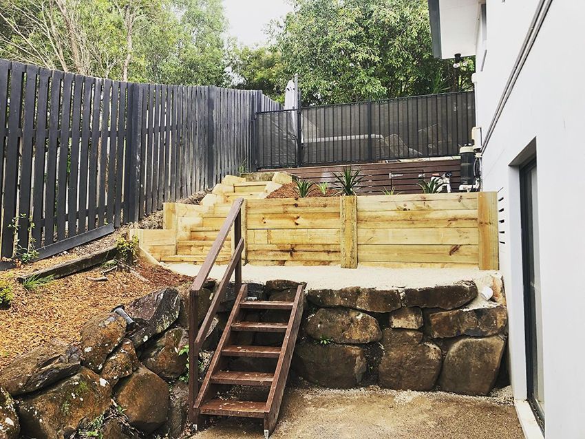 A Wooden Staircase Leading Up to a Rock Wall in a Backyard — HMJ Landscapes in Broadbeach, QLD