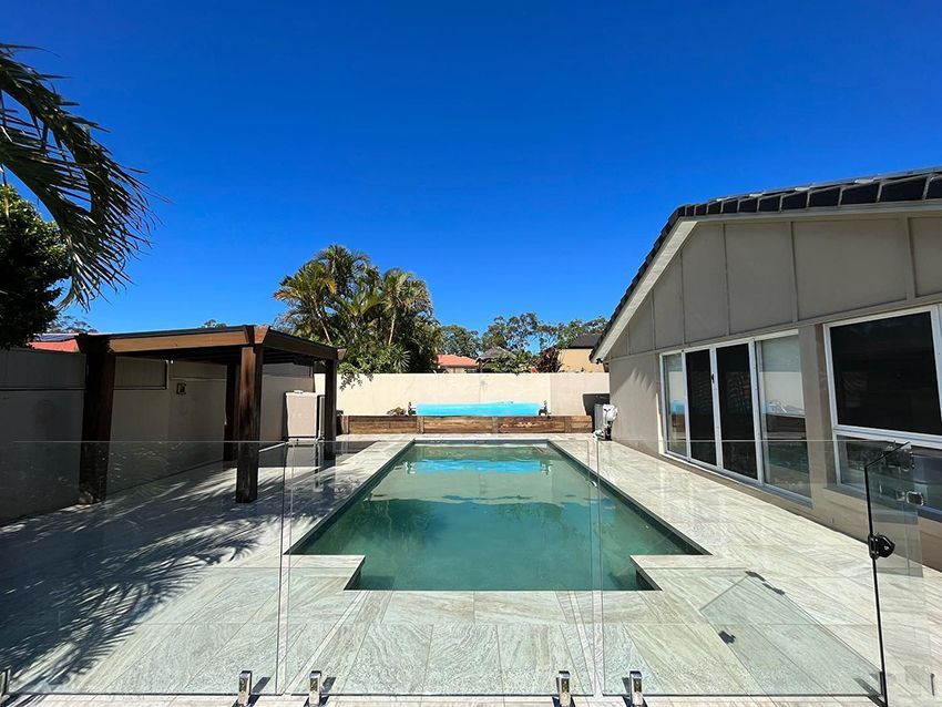 A Large Swimming Pool is Surrounded by a Glass Fence — HMJ Landscapes in Mudgeeraba, QLD