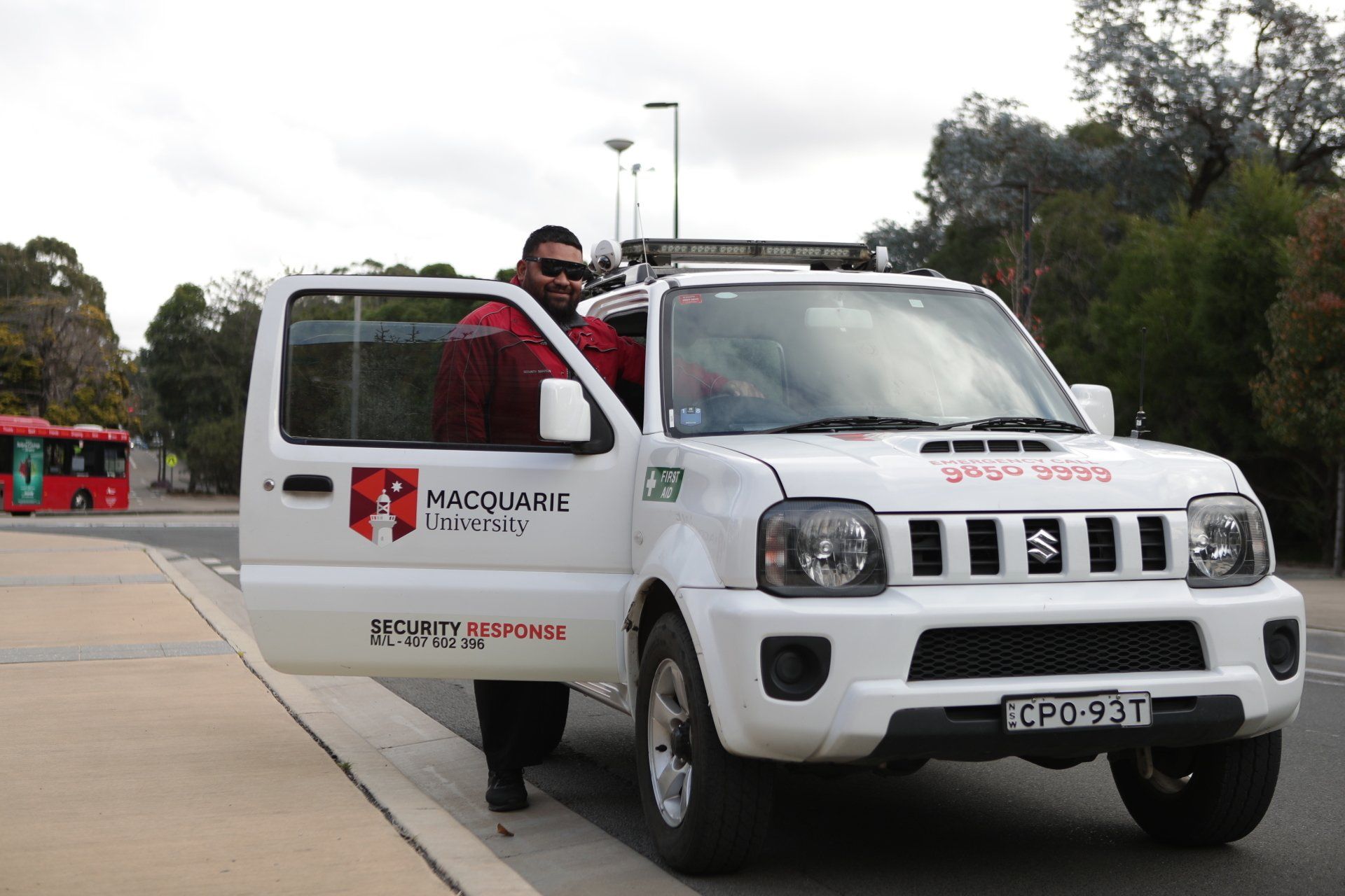 A man in a red jacket is standing next to a white macquarie patrol vehicle