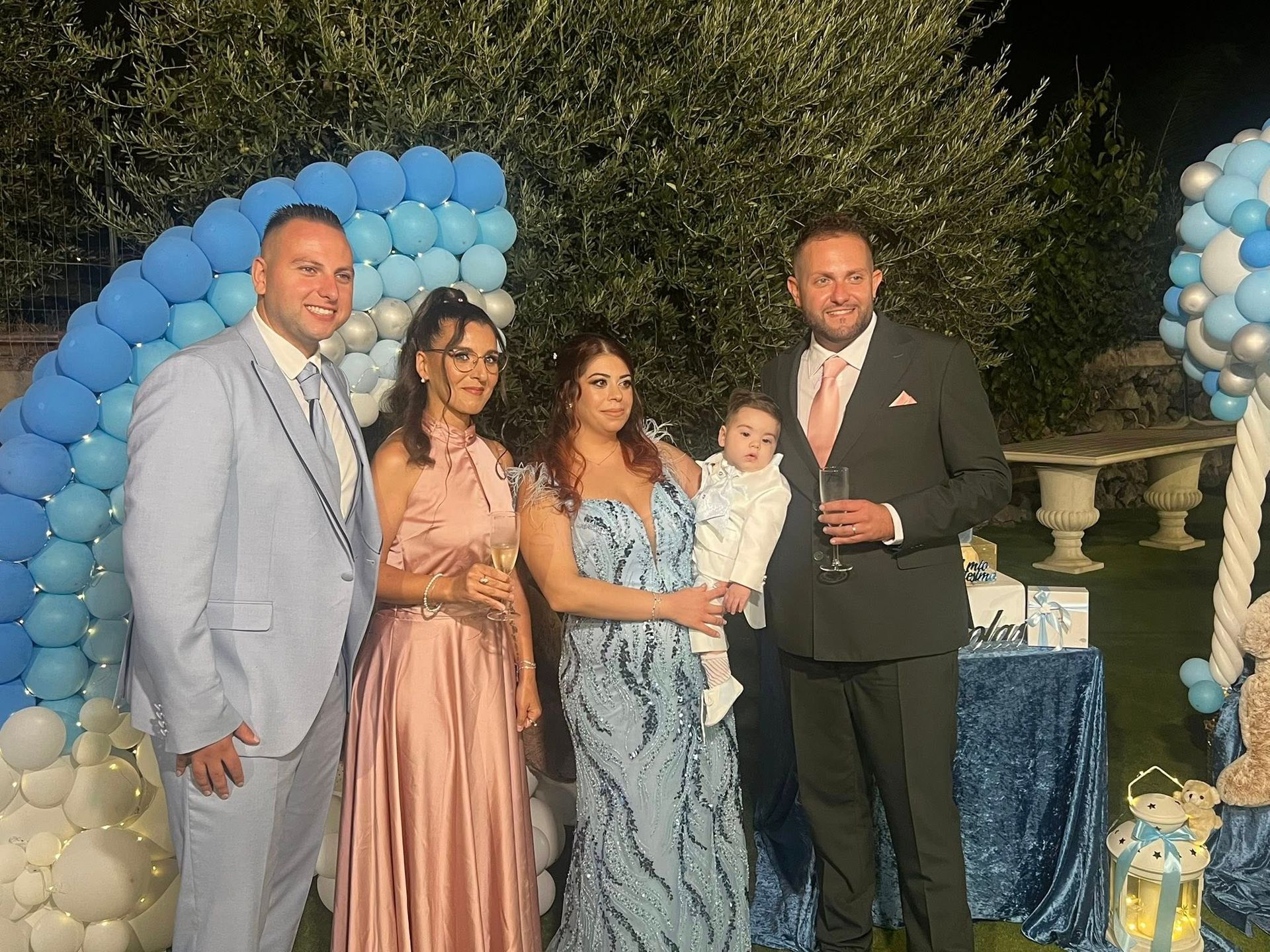 Famiglia che festeggia il compleanno di un neonato. Arco di palloncini blu e bianchi, torta, orsacchiotto.
