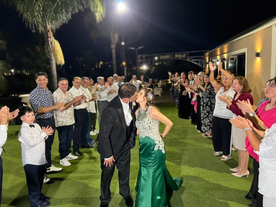 Una coppia si bacia e festeggia con gli ospiti la sera. La sposa indossa un abito verde, lo sposo uno smoking; la gente applaude.