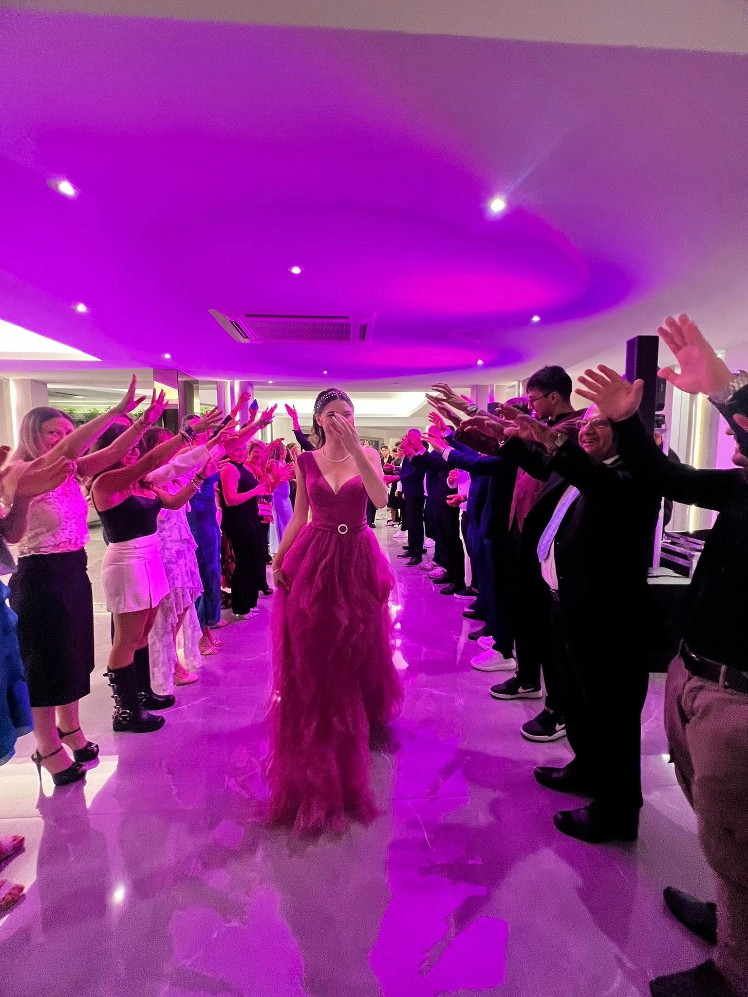 Una donna in abito rosso canta tra file di persone con le braccia alzate in una stanza ben illuminata.