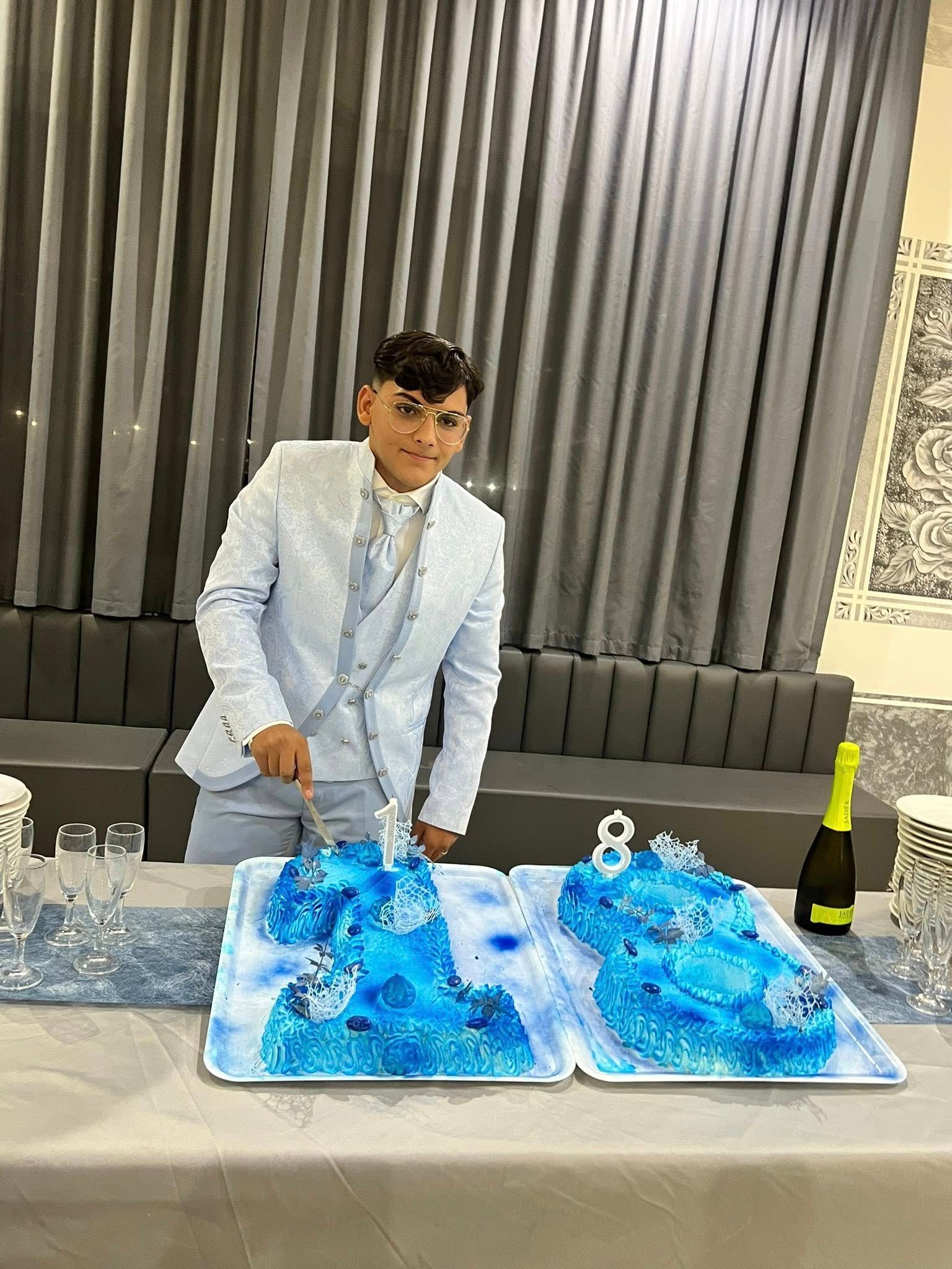 Un uomo in abito blu taglia una torta in due parti decorata con glassa blu durante un evento celebrativo.