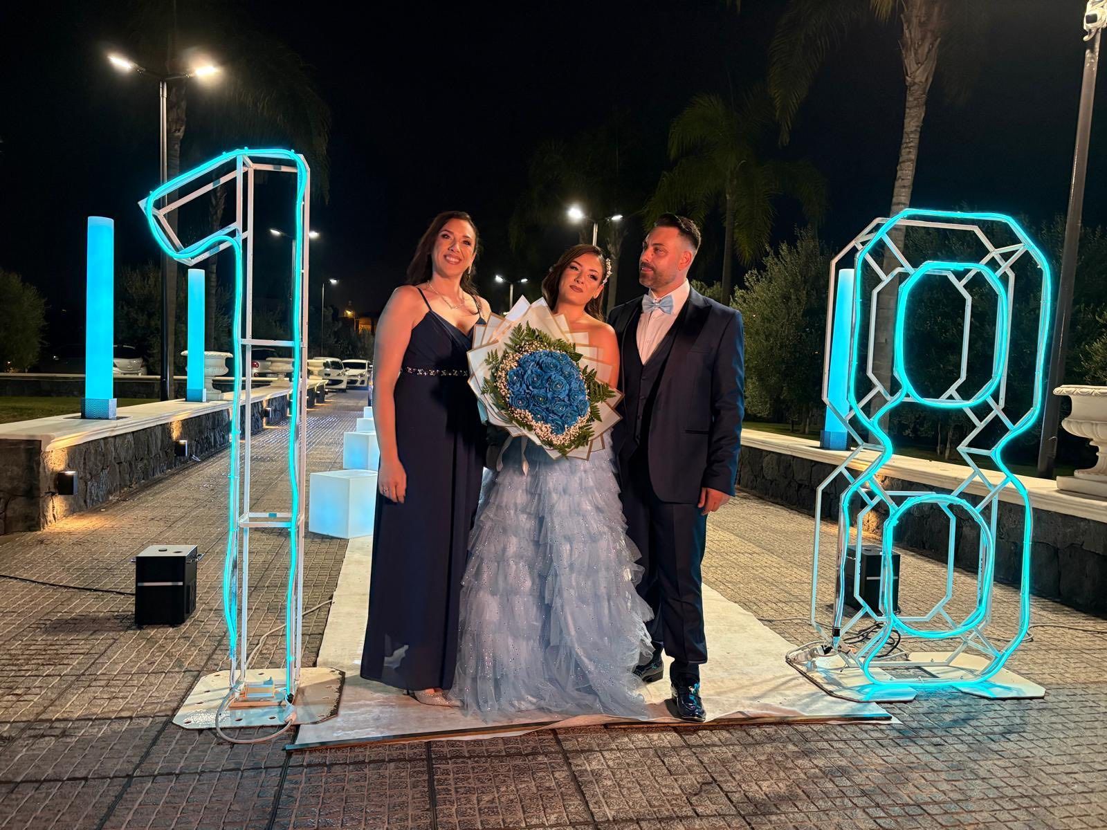 Tre persone posano di notte vicino alle luci al neon con la scritta