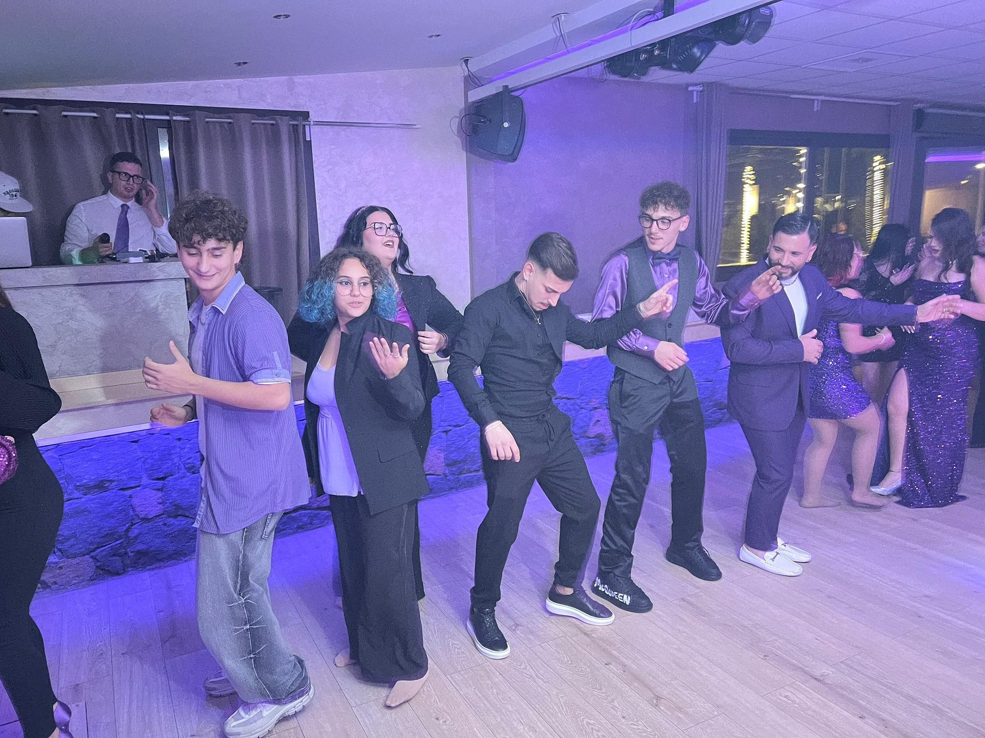 Persone che ballano a una festa con un DJ. Sono vestiti in abiti formali con dettagli viola e neri.