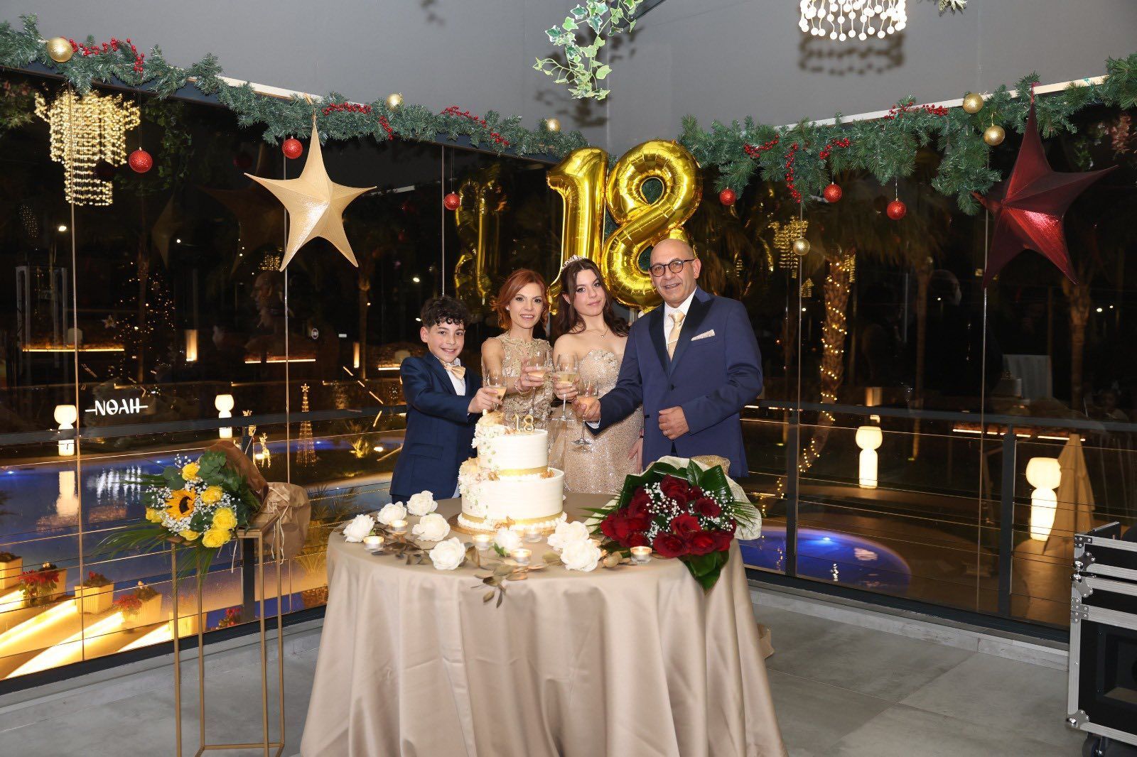 Una famiglia taglia una torta a più piani per una festa di compleanno di 18 anni, decorata con fiori e palloncini.