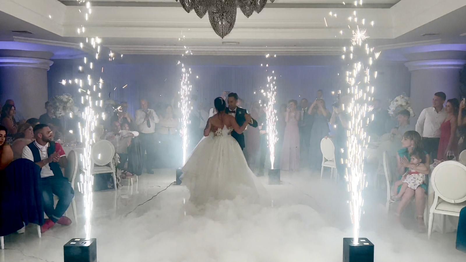 Gli sposi ballano tra scintille e nebbia durante un ricevimento di nozze.