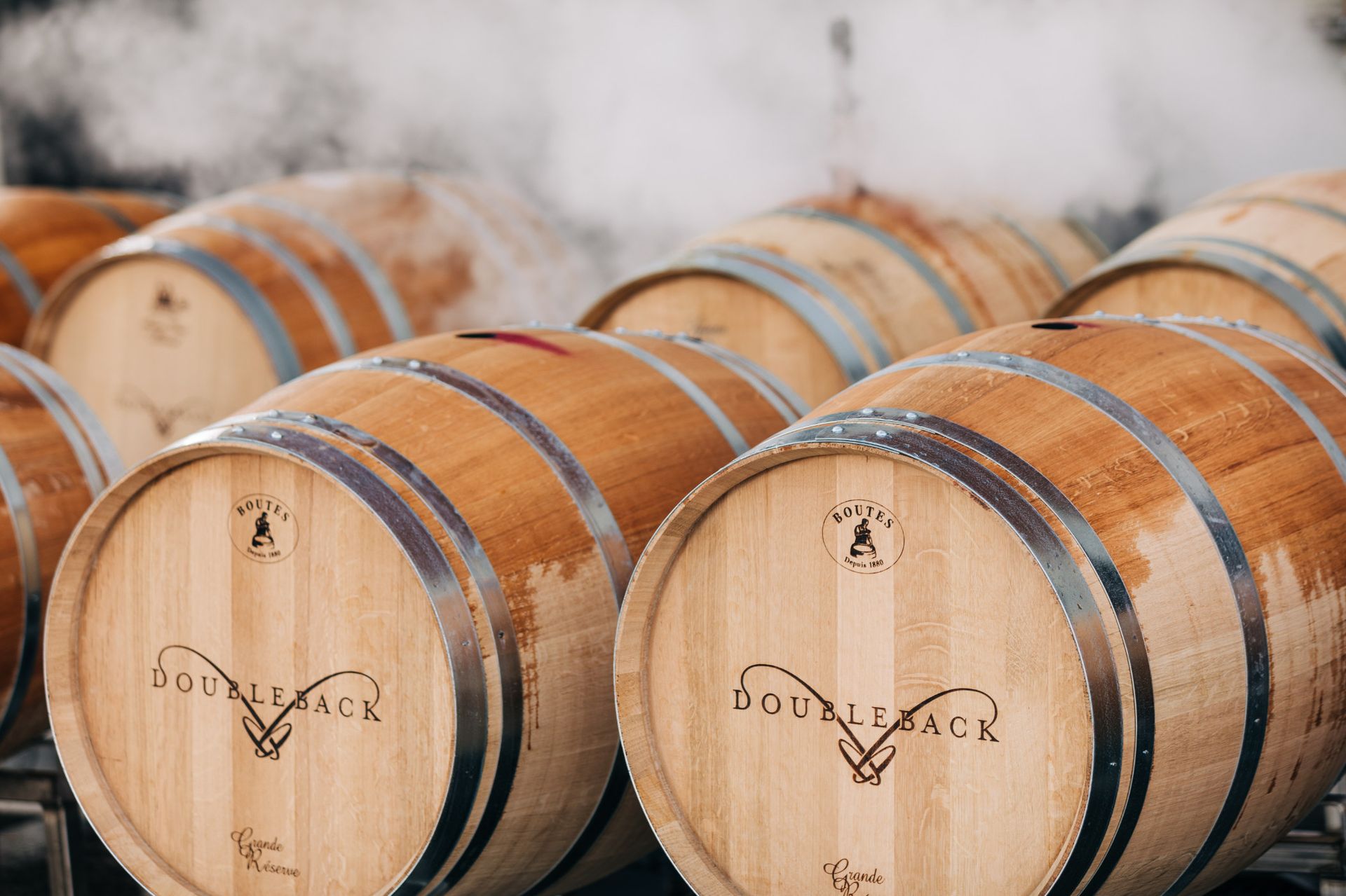 Rows of wooden wine barrels stacked in a cellar with white mist around them