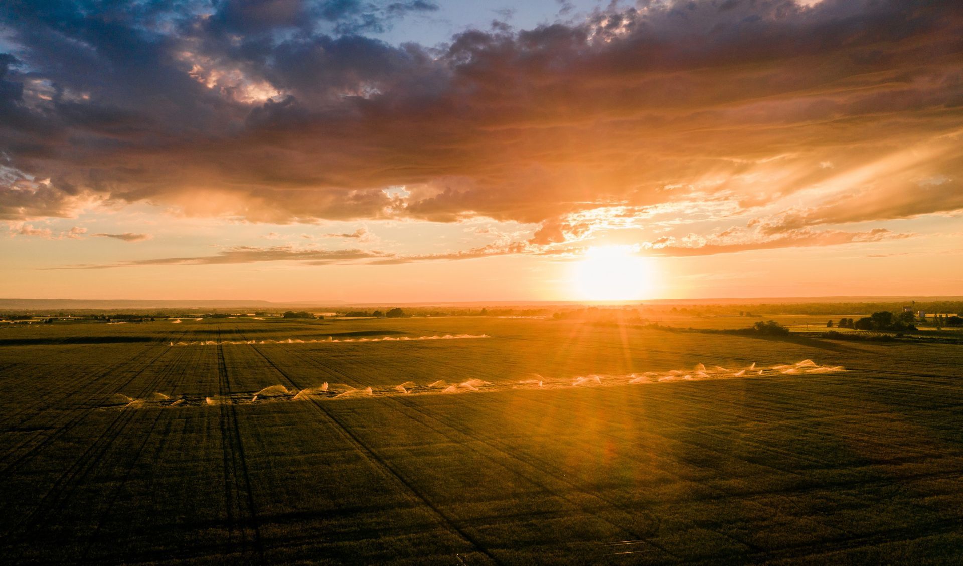 Sunset over a wide green field with dramatic orange clouds and the sun low on the horizon
